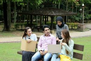 joven asiático malayo chino hombre mujer al aire libre parque libro archivo carpeta ordenador portátil computadora teléfono sentar estar estudiar mezclarse foto