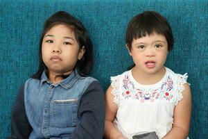 dos pequeño sur este asiático niña niño malayo chino estudiar jugar dibujar utilizar inteligente teléfono en azul tela sofá ellos son autista y abajo síndrome foto