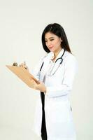 joven asiático hembra médico vistiendo delantal estetoscopio participación escritura en un portapapeles foto