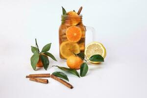 Liquid ice lemon orange tea with slice green leaf cinnamon stick in transparent glass jar mug on white background whole fruit photo