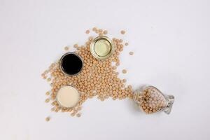 Soya beans flowing out of a hart shape glass bottle soya sauce milk oil in mini glass bowl on white background photo