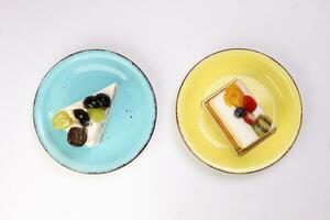 Two slices Green Black Grape Kiwi strawberry blueberry mango fruit cream layer cake pastry on rustic blue yellow round plate over white background photo