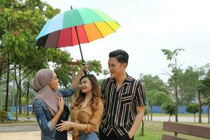 Young Asian Malay man woman outdoor green park walk talk discuss mingle under umbrella photo