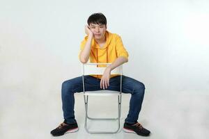 Young good looking Asian chinese malay man pose face body expression mode emotion on white background sit on reversed hand on cheek chair look photo