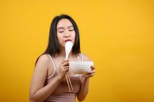 Beautiful young south east Asian woman holding chines empty chopstick Chinese soup spoon bowl utensil pretend acting posing see eat taste smell feed offer satisfaction yummy yellow orange background photo