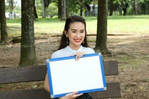 joven asiático chino mujer al aire libre parque instalaciones libro archivo carpeta ordenador portátil computadora teléfono sentar estar estudiar mezclarse foto