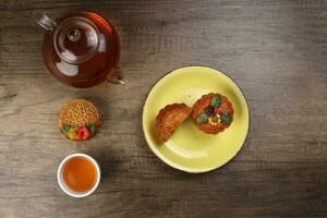 Colourful flower decorated mooncake cut slice half layer Chinese mid autumn festival on glass teapot white ceramic teacup over rustic wood slice cut piece on yellow ceramic plate photo