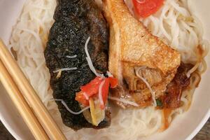 Fish head noodles vermicelli milk soup in white bowl chopstick spoon on rustic wooden background photo