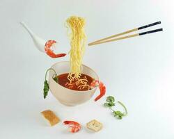 Yellow seafood prawn coriander leaf noodle soup elevated flying suspended in air with soup spoon and chopstick prawn coriander leaf tofu on white background photo