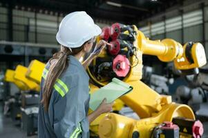 A female engineer checking documented items after installing a program on a robotic arm in a robotic warehouse and test the operation photo