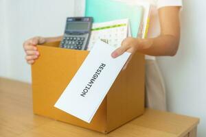 Resignation, Layoff, Unemployment, Dismiss, Job quit, Jobless and Farewell concept. Businesswoman holding letter of Resign contract with documents cardboard box at office photo