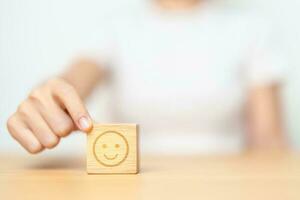 Hand choosing happy face from Emotion block for customer review, good experience, positive feedback, satisfaction, survey, evaluation, assessment, mood and world mental health day concept photo