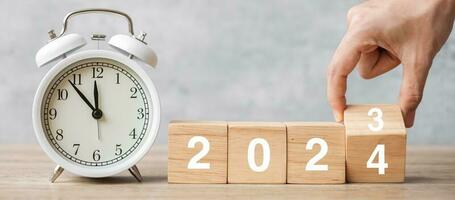 Happy New Year with vintage alarm clock and hand flipping 2023 change to 2024 block. Christmas, New Start, Resolution, countdown, Goals, Plan, Action and Motivation Concept photo