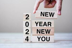 hand holding wooden block with text 2024 NEW YEAR NEW YOU on table background. Resolution, strategy, goal, business and holiday concepts photo