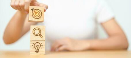 Woman hand holding dartboard above magnifying and Lightbulb icon block. business planning process, goal, vision, strategy, target, mission, action, research, teamwork and idea concept photo