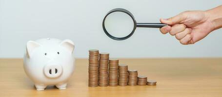 Money saving, Inflation, tax, cash flow, Job search, hiring and research development concepts. coins money stack growing with magnifier glass and piggy bank on table photo