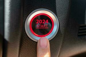 Finger press a car ignition button with 2024 START text inside  automobile. New Year New You, forecast, resolution, motivation, change, goal, vision, innovation and planning concept photo