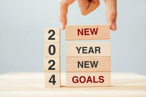 hand holding wooden block with text 2024 NEW YEAR NEW GOALS on table background. Resolution, strategy, solution, business and holiday concepts photo