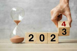hand flipping block 2023 to 2024 text with hourglass on table. Resolution, time, plan, goal, motivation, reboot, countdown  and New Year holiday concepts photo