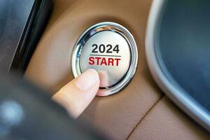 Finger press a car ignition button with 2024 START text inside  automobile. New Year New You, forecast, resolution, motivation, change, goal, vision, innovation and planning concept photo