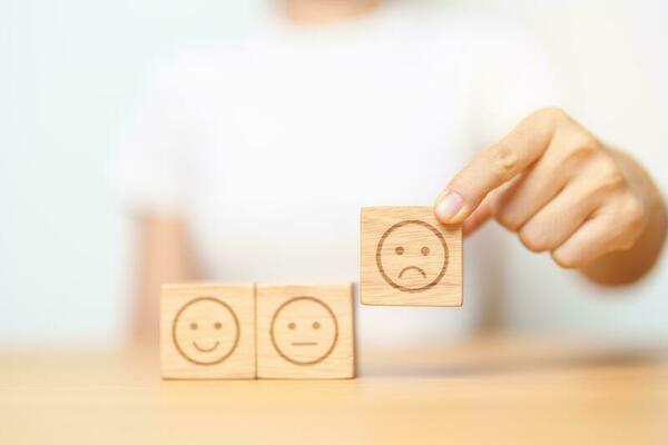 Hand choosing unhappy angry face from Emotion block. customer review, bad experience, negative feedback, satisfaction, survey, rating service, assessment, mood, world mental health day concepts