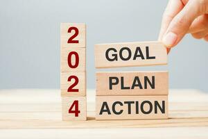 hand holding wooden block with text 2024 GOAL, PLAN and ACTION on table background. Resolution, strategy, solution, goal, business and New Year holiday concepts photo