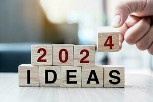 Businessman hand holding wooden cube with flip over block 2023 to 2024 Plans word on table background. Resolution, strategy, solution, goal, business and New Year holiday concepts photo