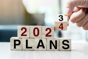 Businessman hand holding wooden cube with flip over block 2023 to 2024 Plans word on table background. Resolution, strategy, solution, goal, business and New Year holiday concepts photo