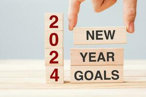 hand holding wooden block with text 2024 NEW YEAR NEW GOALS on table background. Resolution, strategy, solution, business and holiday concepts photo