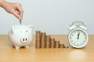 Money Saving for Future Plan, Retirement fund, Pension, Investment, Wealth Business and Financial concepts. hand putting coin into piggy bank with clock, Counting and stack arrangement for deposit photo