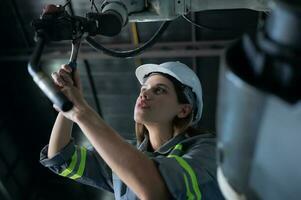 Female Technician Inspecting and repairing robotics arm in robots hangar and test the operation of the machine after being used for a while, as well as updating the software and calibration photo