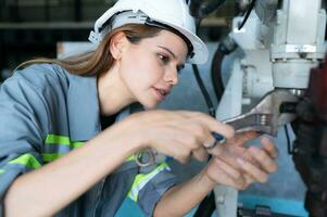 Female Technician Inspecting and repairing robotics arm in robots hangar and test the operation of the machine after being used for a while, as well as updating the software and calibration photo
