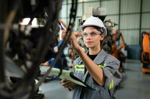 A female engineer checking documented items after installing a program on a robotic arm in a robotic warehouse and test the operation photo