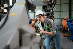 A female engineer checking documented items after installing a program on a robotic arm in a robotic warehouse and test the operation photo