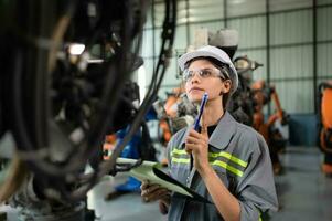 A female engineer checking documented items after installing a program on a robotic arm in a robotic warehouse and test the operation photo