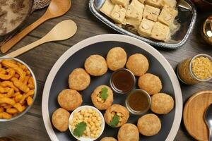 verity of indian bengali street food tea time snacks onion pakoda crunchy spicy lentils moong dal fry sweet shompapri chaat pani puri fuska on rustic retro table plate brass copper pots silver tray photo