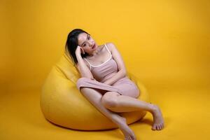 hermosa joven sur este asiático mujer sentar en un amarillo naranja bolsa de frijoles asiento color antecedentes relajarse descanso pensar emoción imagina expresión actitud foto