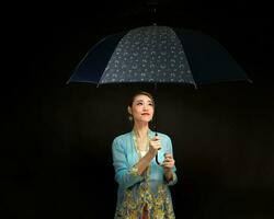 asiático mujer en traccional kebaya que lleva paraguas en negro antecedentes foto