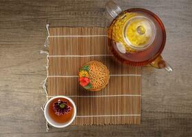 Colourful flower decorated mooncake Chinese mid autumn festival on bamboo food mat white background slice cut piece layered on yellow ceramic plate glass teapot teacup top view photo