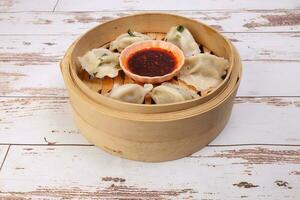 Home style dim sum dumpling in bamboo steamer chili flake oil sauce on rustic wooden background photo