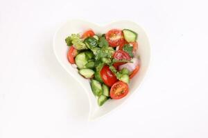 Indian Subcontinent style tomato cucumber onion chili coriander salad in hart shape white dish on white background photo