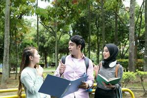 Young asian malay chinese man woman outdoor park walk stand study talk discuss point laptop file book backpack mingle photo