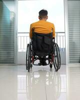 Young man south east Asian malay origin sitting on wheelchair looking outside balcony window. Paralyzed waist down due to accident photo