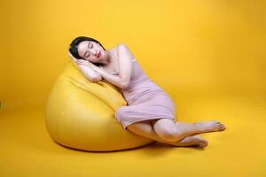 Beautiful young south east Asian woman sit on a yellow orange beanbag seat color background relax rest think emotion imagine expression pose sleep photo