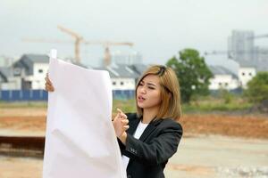 mujer chino malayo trabajador ingeniero administración a construcción sitio leyendo viendo plan foto