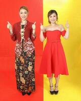 Two Asian woman traditional kebaya and modern dress red yellow paper background thumbs up photo