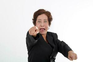 Elderly asian Chinese female on white background wearing black suit point at camera angry furious mouth open shout photo