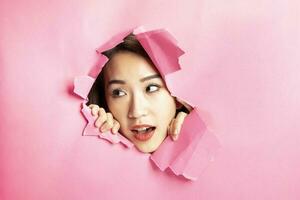 Young beautiful Asian woman expression through torn paper hole photo