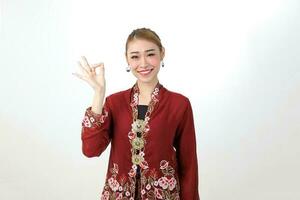 Asian woman traditional red maroon kebaya sharong on white background showing ok finger sign photo