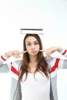 Yong Asian youth girl in casual dress balancing book on head look at camera finger on cheek expression mouth blown funny face on white background photo